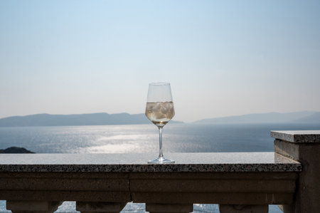 A wine glass with ice cubes stands on a balcony railing with a blue sky ,sea and islandの写真素材