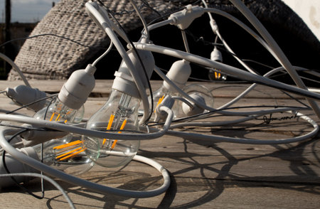 Two lightbulbs with yellow filaments are surrounded by messy electrical wires on a wooden tableの写真素材