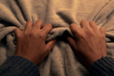 Two wounded hands are angrily squeezing a blanketの写真素材