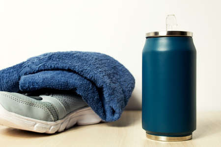 Blue thermos with a towel and sneakers on a light background.