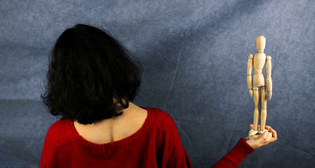 A woman in a red sweater holds a wooden mannequin.の写真素材