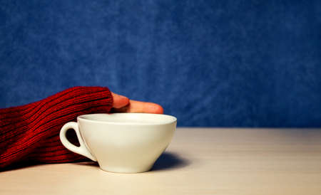 Cup of hot drink with hand in red knitted sweater on wooden tableの写真素材