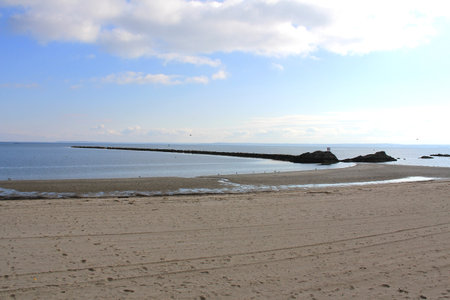 Sandy beach with a rock pier leading into the water on an overcast day with dramatic light and clouds at the late afternoon.の写真素材