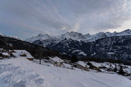Tranquility scene after sunset of a mountain village in front of a snowcapped mountain range in Switzerland.の写真素材