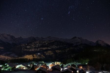 Tranquility scene at midnight of a enlightened mountain village in front of a snowcapped mountain range in Switzerland.の写真素材