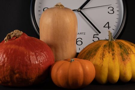 Cropped section of an arrangement with a white clock, red pumpkin, a mini orange pumpkin, butternut and a yellow pumpkin with black background, closeup.の写真素材