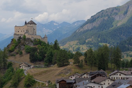 Small mountain village and a Castle on the top of a natural hill at cloudy day with swiss mountain panorama in background.のeditorial素材