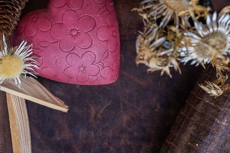 Valentine's day, rustic pink flowered heart with straw flowers and kindling on leather background. High angle view, for text.の写真素材
