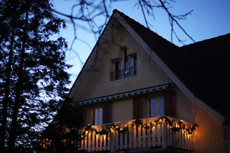 Christmas wreaths with candle lights on wooden balcony in the dusk at Christmastime. Tree at left...
