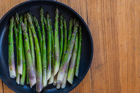 Fried green asparagus in black pan on wooden background. Top view, copy space.の写真素材