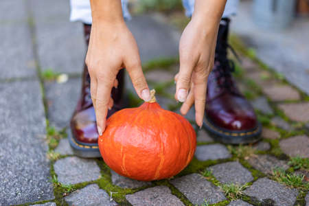 close up of hands and boots of a young woman, who lifts up an orange pumpkin.の写真素材