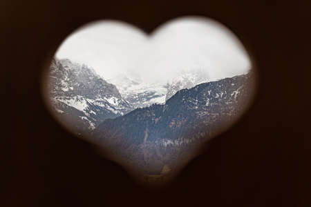 View to snowy Swiss alps in winter through heart shape of wooden plank.の写真素材