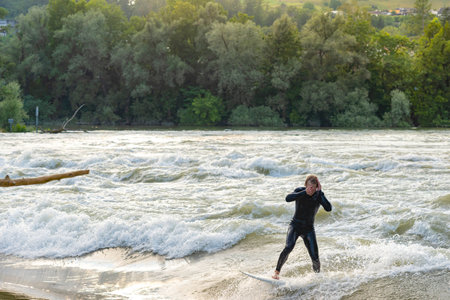 During the flood, a young surfer with neoprene wetsuit, is seen by the Aare river, wiping his face after braving the abundance of water.の写真素材