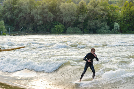 A young surfer wearing a wetsuit surfs in the Aare river during high tide.