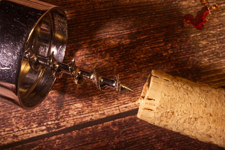 Metal corkscrew and cork on wooden background.