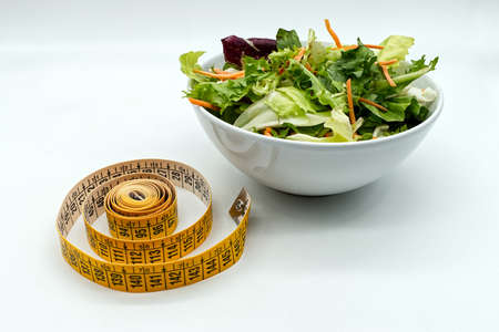 Fresh salad in a bowl and measuring tape. Diet and healthy eating concept.の写真素材