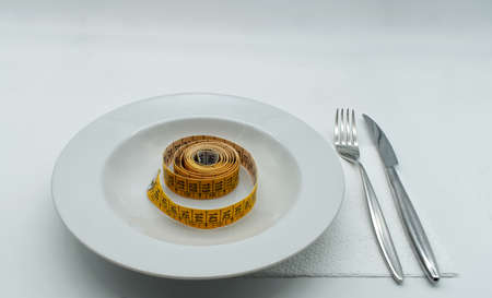 Yellow measuring tape in empty white plate. Diet and weight loss concept.の写真素材