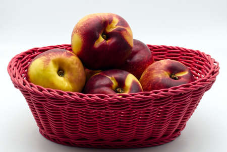 Ripe peaches in a red basket isolated on white background
