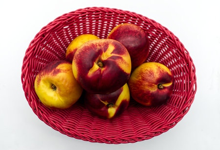 Ripe peaches in a red basket isolated on white backgroundの写真素材