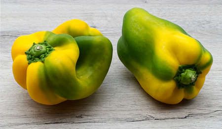 Fresh raw half green and half yellow sweet bell peppers on wooden table.の写真素材