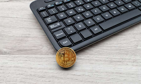 Golden Bitcoin next to a black computer keyboard. New technological economy concept.の写真素材