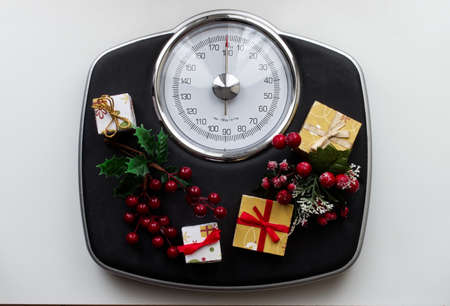 Analog scale surrounded by Christmas decorations and gifts. Overweight left after Christmas holidays. Start diet concept.の写真素材