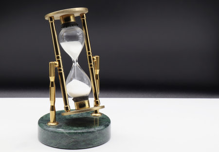 Hourglass on white table isolated on black background. Time passing concept