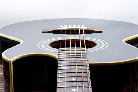 Acoustic black guitar on wooden table and white background.