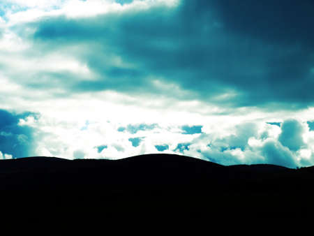 Dramatic scene of clouds behind a dark hill silhouetteの写真素材
