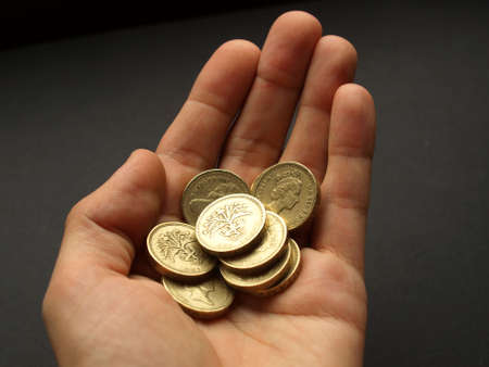 Hand with British Pounds coins (UK currency) over a dark backgroundの写真素材
