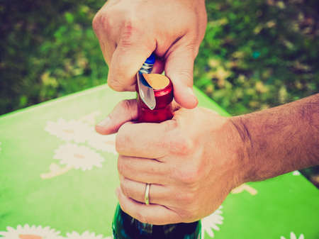 Vintage looking Hand opening a bottle of wine on a tableの写真素材