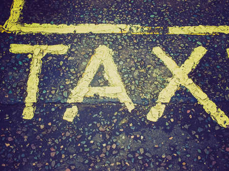 Vintage looking Tax sign in yellow over gray asphalt backgroundの写真素材
