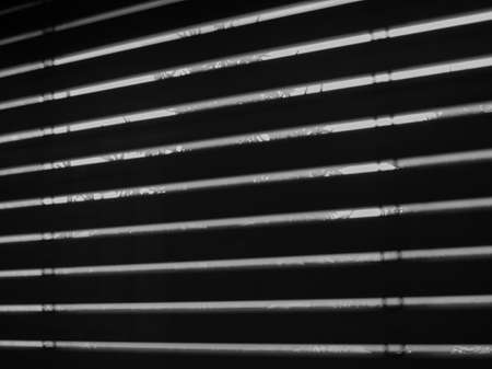 Silhouette of windows blinds seen from a dark room against the sun lightの写真素材