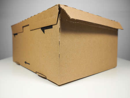 Small brown packet corrugated cardboard parcel for mail shipping on a white table with elegant grey...