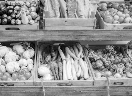 Vegetables on a market shelf including courgettes cabbage tomatos turnips carrots garlic and red onions in black and whiteの写真素材