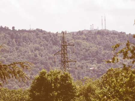 An electric power high voltage transmission line - selective focus on mast, with tv radio and mobile antenna aerial on background hill vintageの写真素材