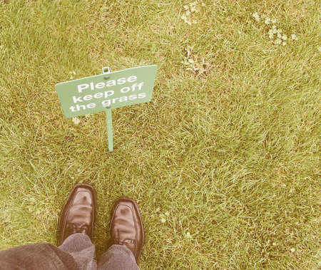 Keep off the grass sign in a meadow, with feet breaking the law vintage