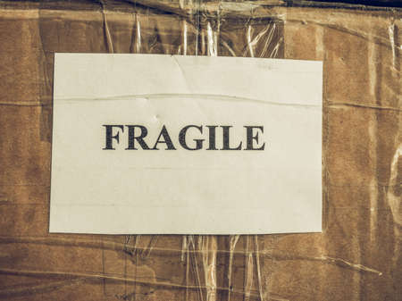 Vintage looking Fragile warning label tag on a cardboard box packet parcel for mail post shipping