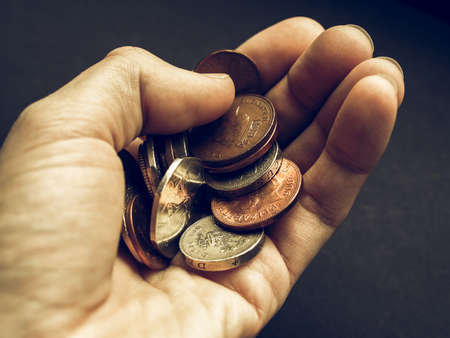 Vintage looking Hand with British Pounds coins (UK currency) over a dark backgroundの写真素材