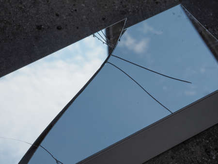 cracked mirror reflecting blue sky with cloudsの写真素材