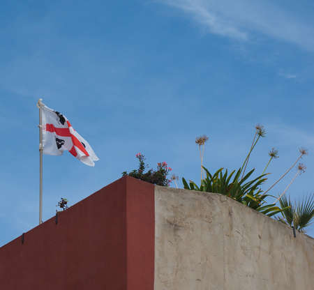 flag of Sardinia (aka flag of the Four Moors) on the top of a wall, over blue skyの写真素材