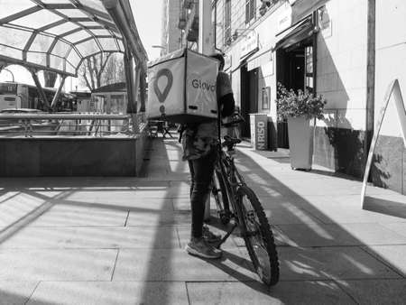TURIN, ITALY - CIRCA FEBRUARY 2019: Glovo courier delivering food and products in black and white