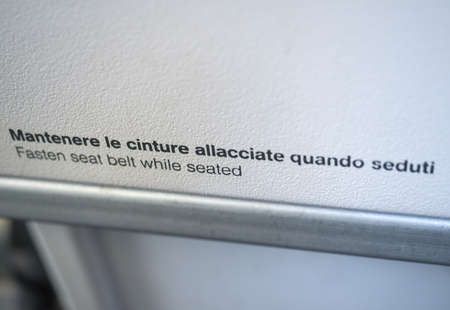 aircraft safety sign in Eglish and Italian: fasten seat selt while seated, mantenere le cinture...