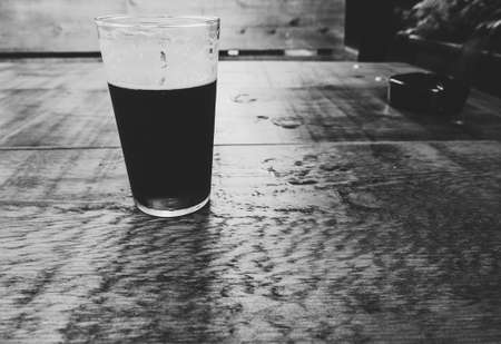 a pint of British ale beer and an ashtray on a wooden pub table in black and whiteの写真素材