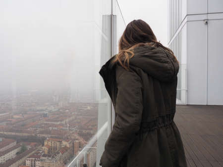 TURIN, ITALY - CIRCA DECEMBER 2019: girl looking down at cityscape from skyscraper
