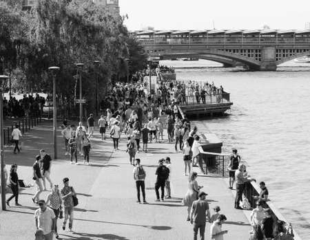 LONDON, UK - CIRCA SEPTEMBER 2019: People walking down the sidewalk on the bank of River Thames in black and whiteの写真素材