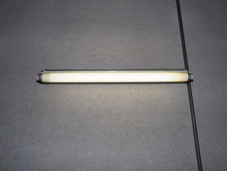 lit fluorescent light bulb over concrete wall backgroundの写真素材