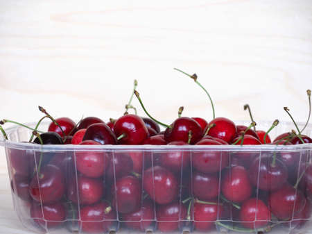 red cherries in a plastic basket on wooden tableの写真素材
