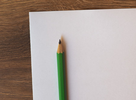 green pencil on blank paper sheet on wooden desktop with copy spaceの写真素材
