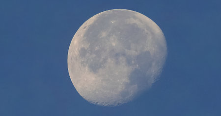Full moon seen with astronomic telescope over blue sky in the morningの写真素材